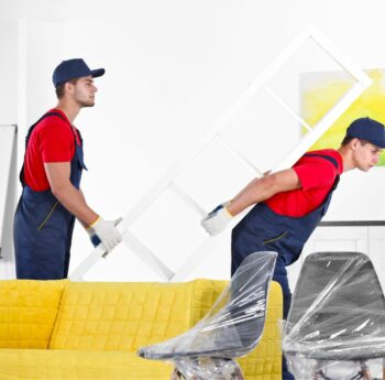Zwei Helfer tragen ein Möbelstück an einem gelben Sofa vorbei