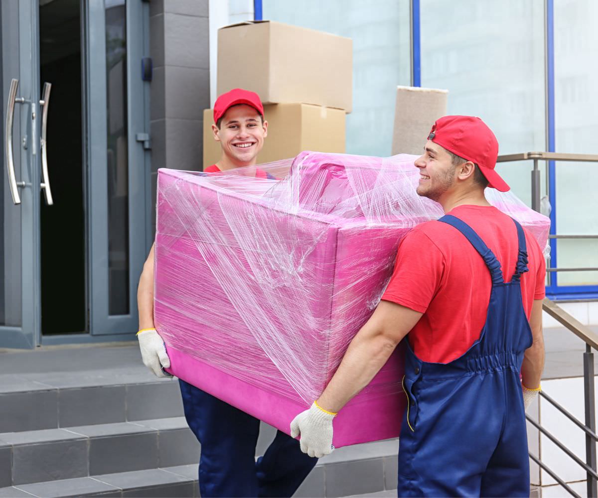 Möbeltransport: Zwei Umzugshelfer tragen ein in Folie gepacktes Möbelstück